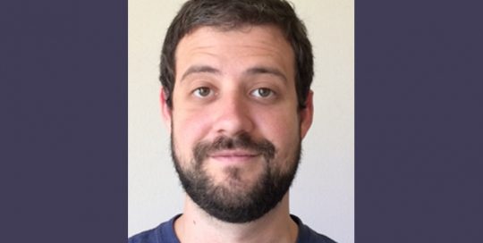 Headshot photo of a man in a blue T shirt_