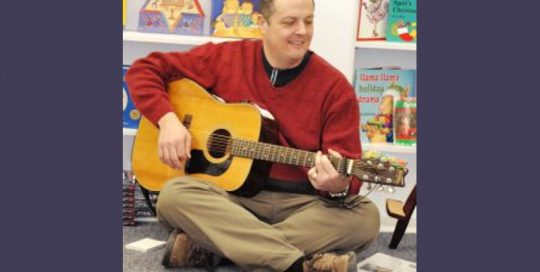 a man wearing a red sweater is playing a guitar