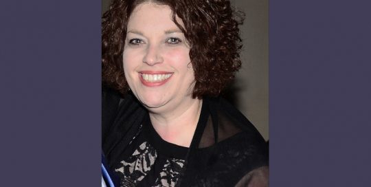 Headshot of a woman in a black top and with curly hair_Traci Solomon