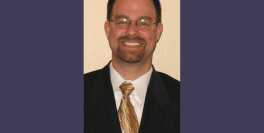 Headshot Photo of a Man in a Black Coat Smiling_